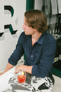 Man relaxing at the front of a bar, drink in hand, wearing a navy Signature Terry Towelling Long Sleeve Polo by Hapeto.