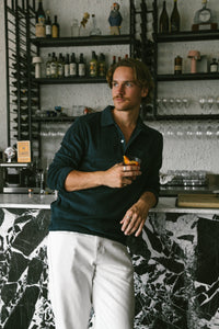 Man leaning on a bar, drink in hand, wearing a navy Signature Terry Towelling Long Sleeve Polo by Hapeto.