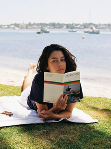 A women lounging near the water while wearing terry towelling polo shirt in navy